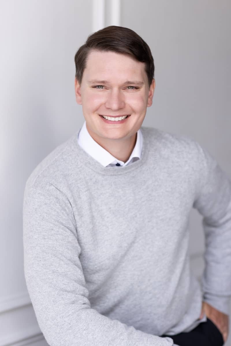 Portrait of Aaron smiling in a gray sweater against a light background
