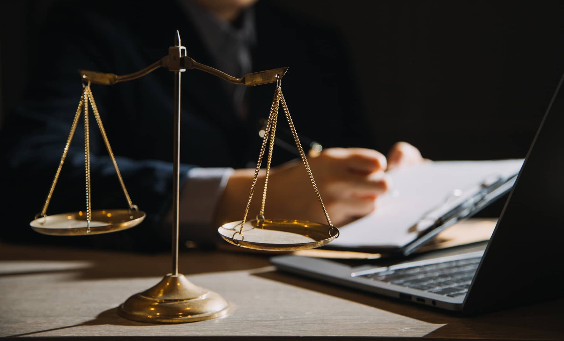 Golden scales of justice on a desk beside a person writing next to a laptop