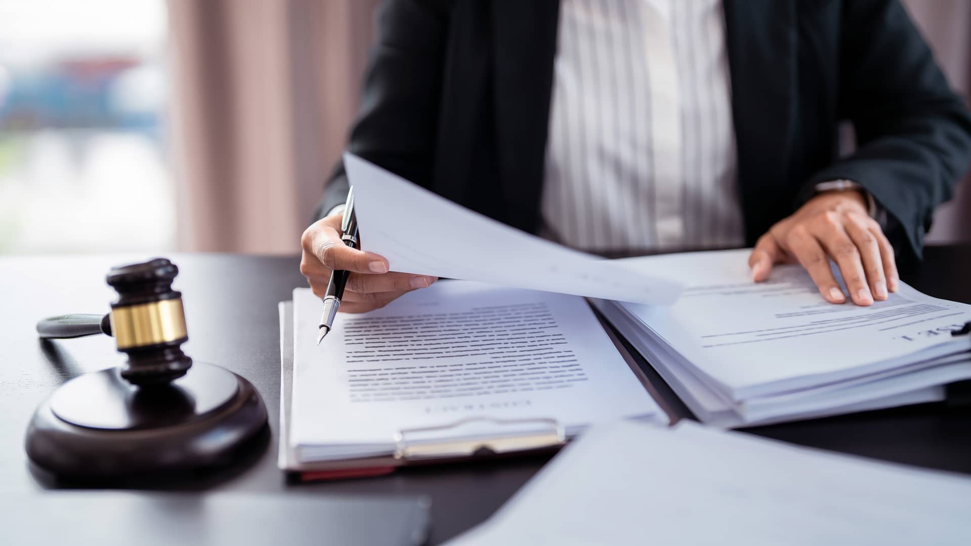 Person in a suit signing legal documents beside a wooden gavel on a desk